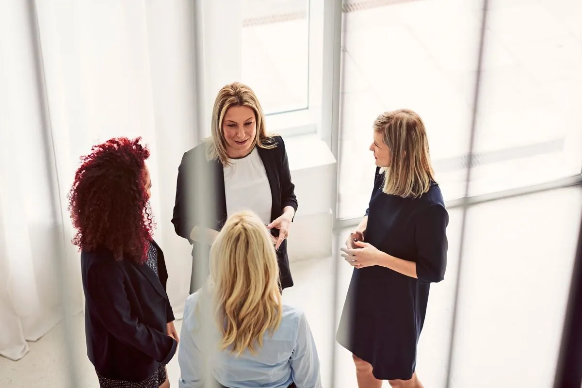 Vier professionell gekleidete Frauen stehen im Kreis und unterhalten sich